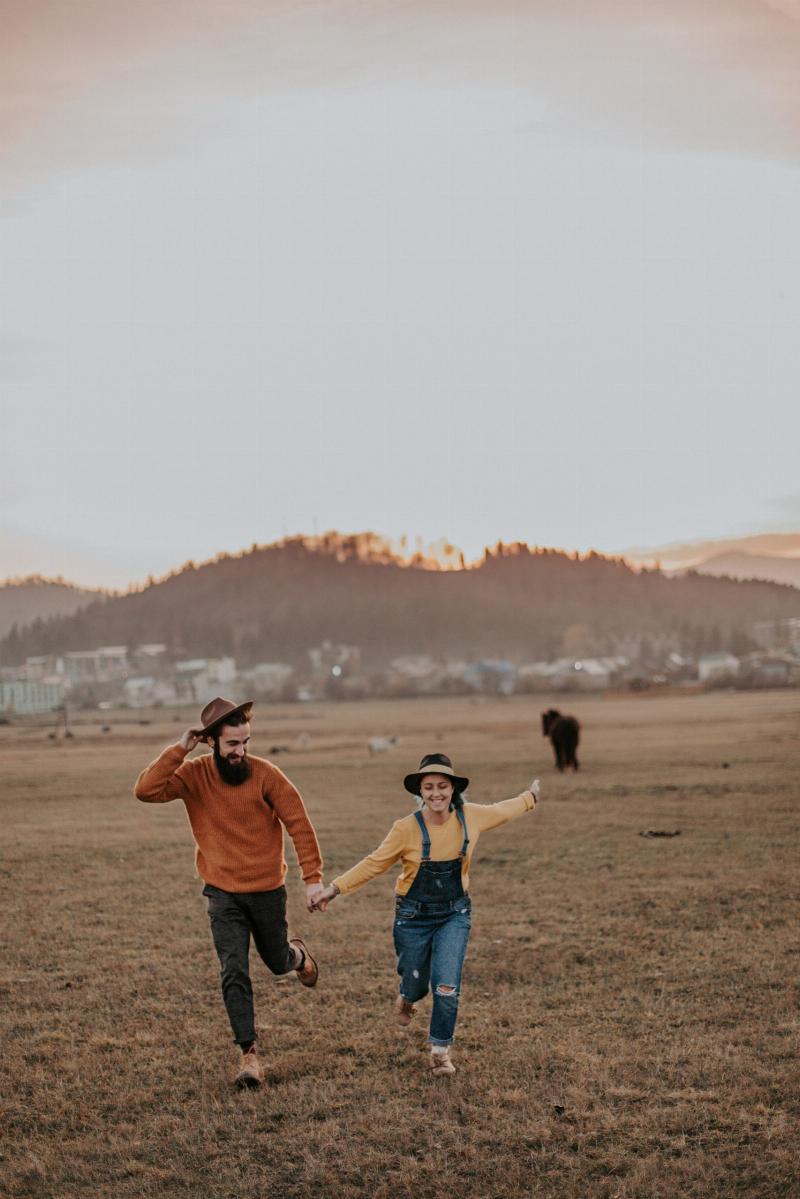 man and woman run holding hands on grass