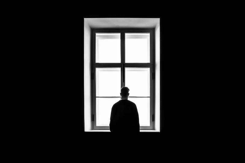 man stands facing a window in complete darkness
