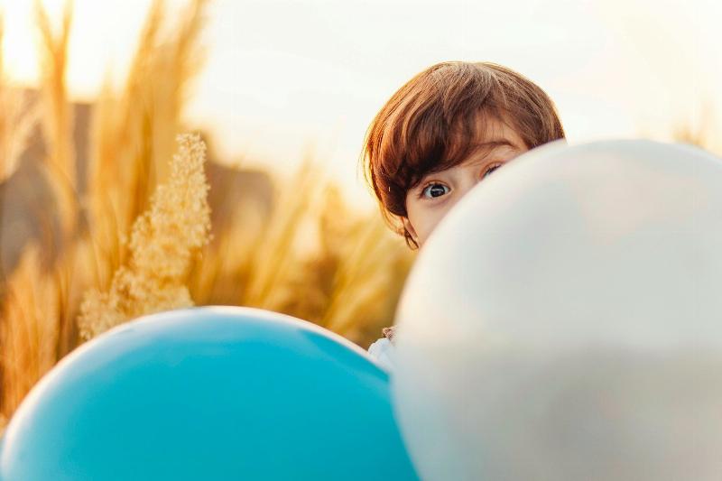 Little kid popping up behind balloons in a field