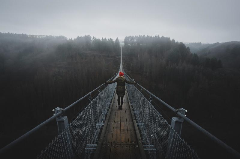 woman walking across hanging bridge in the fog