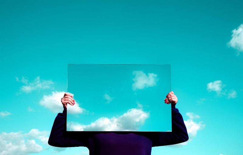 person holding mirror reflecting the sky