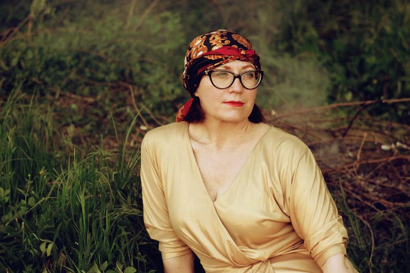 Mature woman looks off to the sie while wearing headscarf and sitting on grass