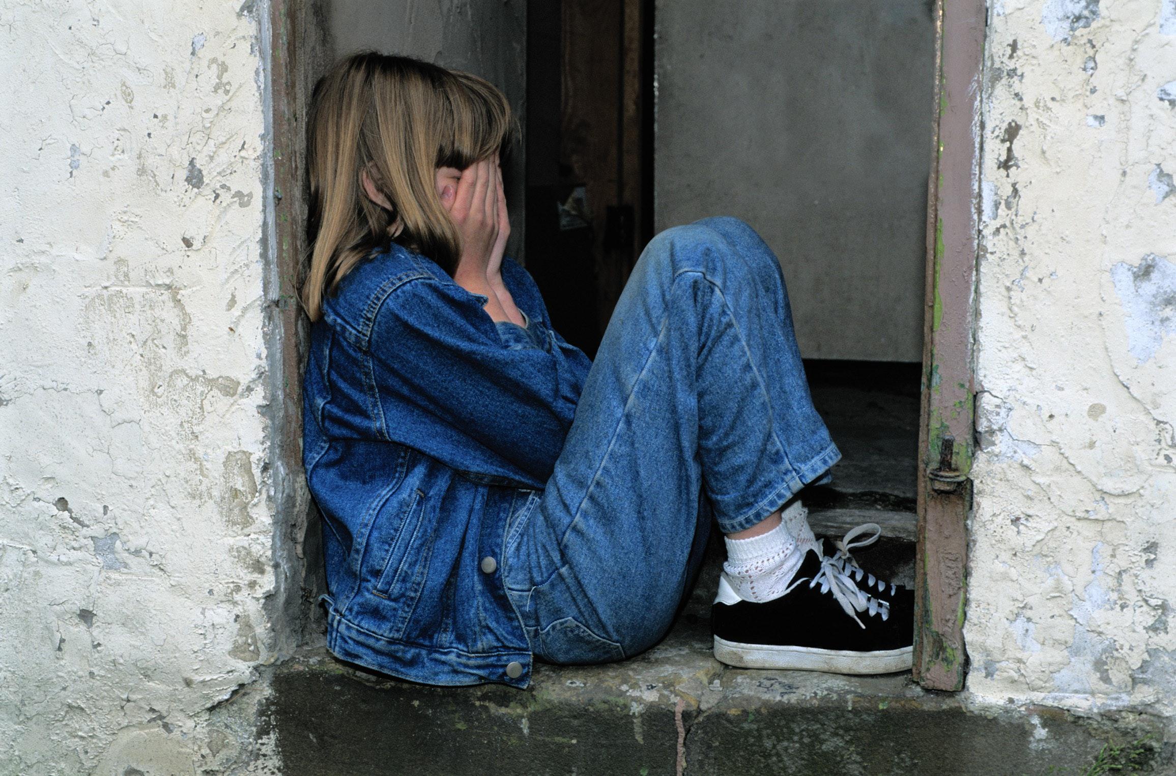young girl sits in doorway crying into her hands