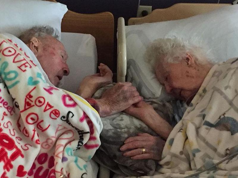old couple reach for each other's hands in hospital bed