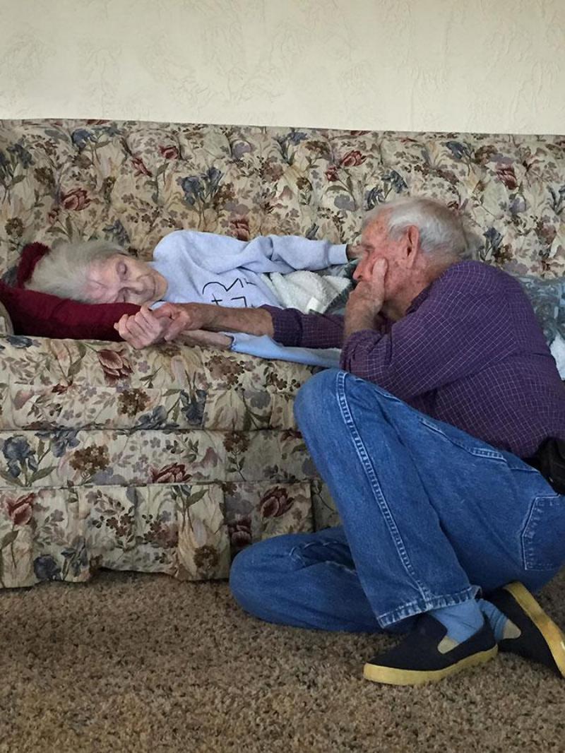 woman lays on couch as elderly man sits on the floor and holds her hand