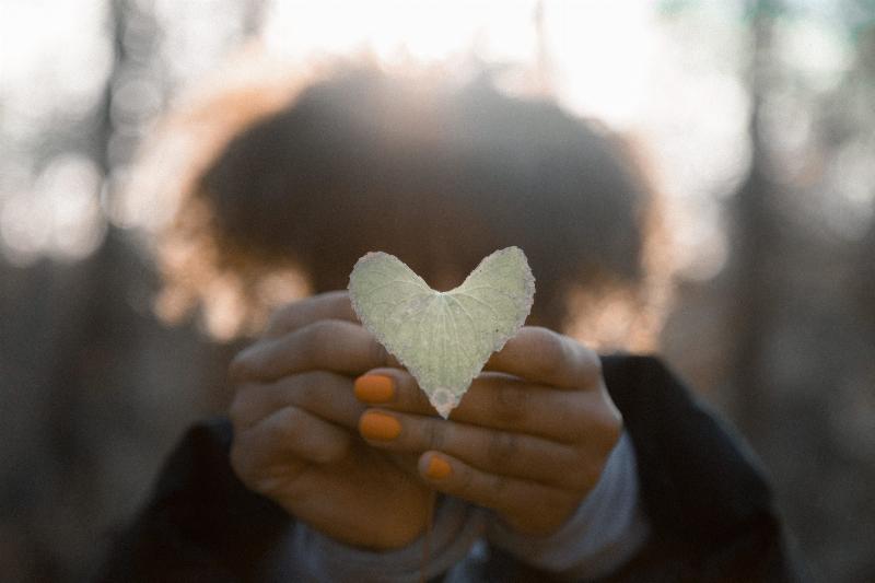woman holds heart shaped leaf to camera