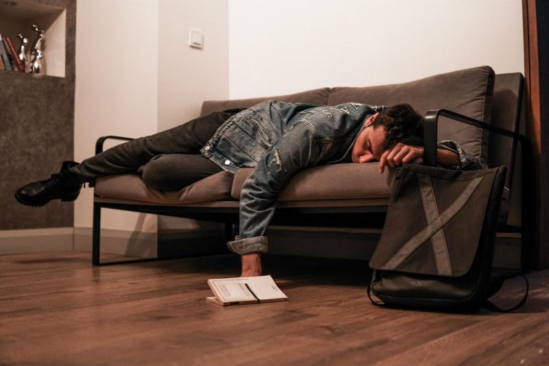 man lays on couch asleep with book on the floor