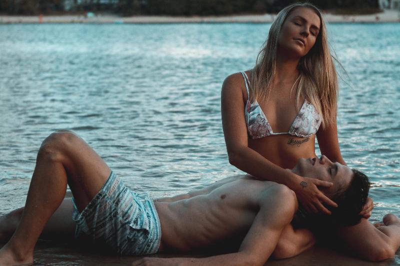 woman sits in bikini with man laying on her legs