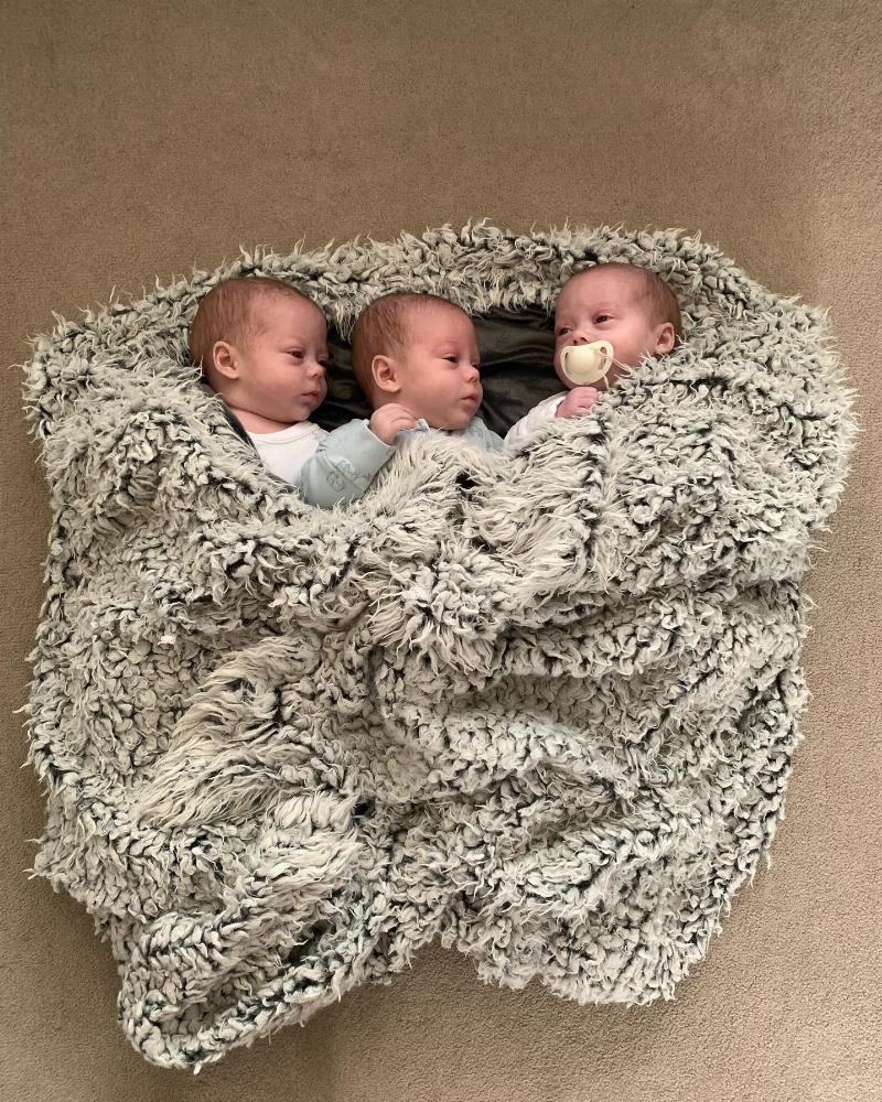 triplets wrapped up in grey blanket