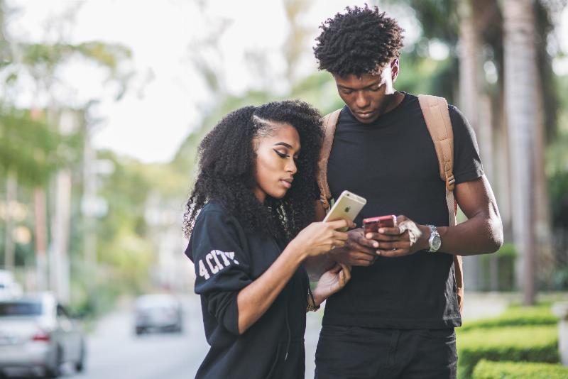 man and woman standing on street and looking down at their phones