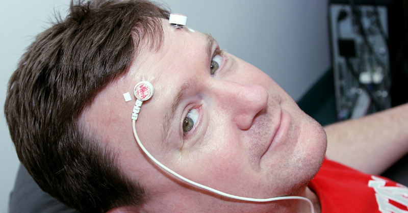 man hooked up to wires on his temples and looking up to the camera