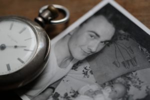 black and white photo of man holding baby beside clock