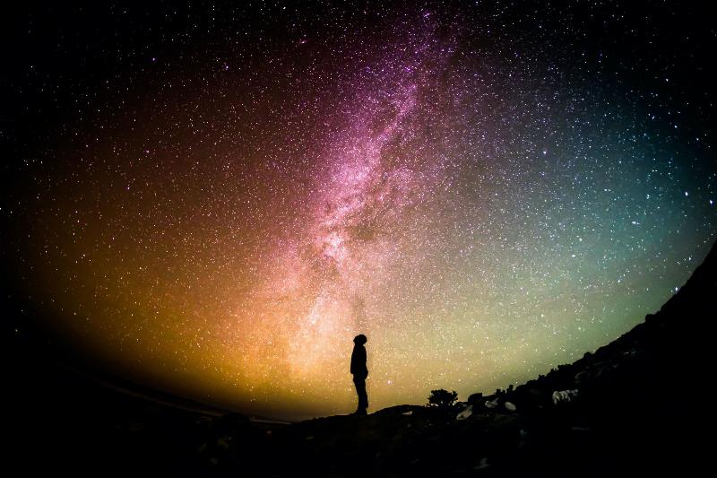 man's silhouette stands looking up at the starry universe