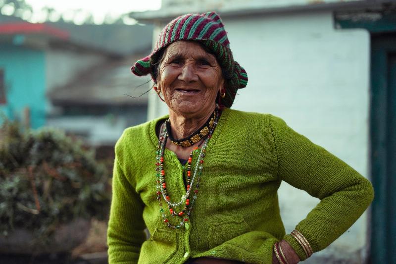 older woman poses in green cardigan and smiles outside