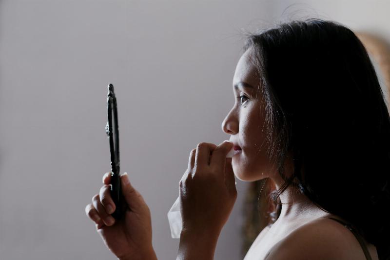 woman looks in handheld mirror to wipe the lipstick