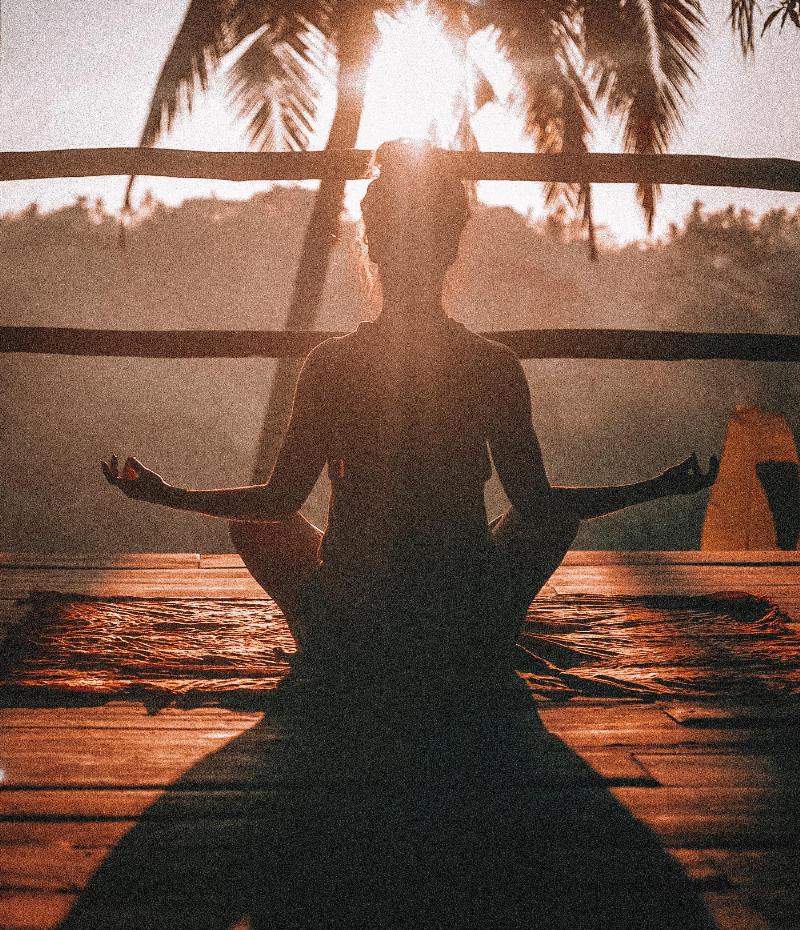 woman meditating while facing the sun on a deck