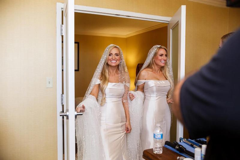 twin sisters in wedding gowns walking through door