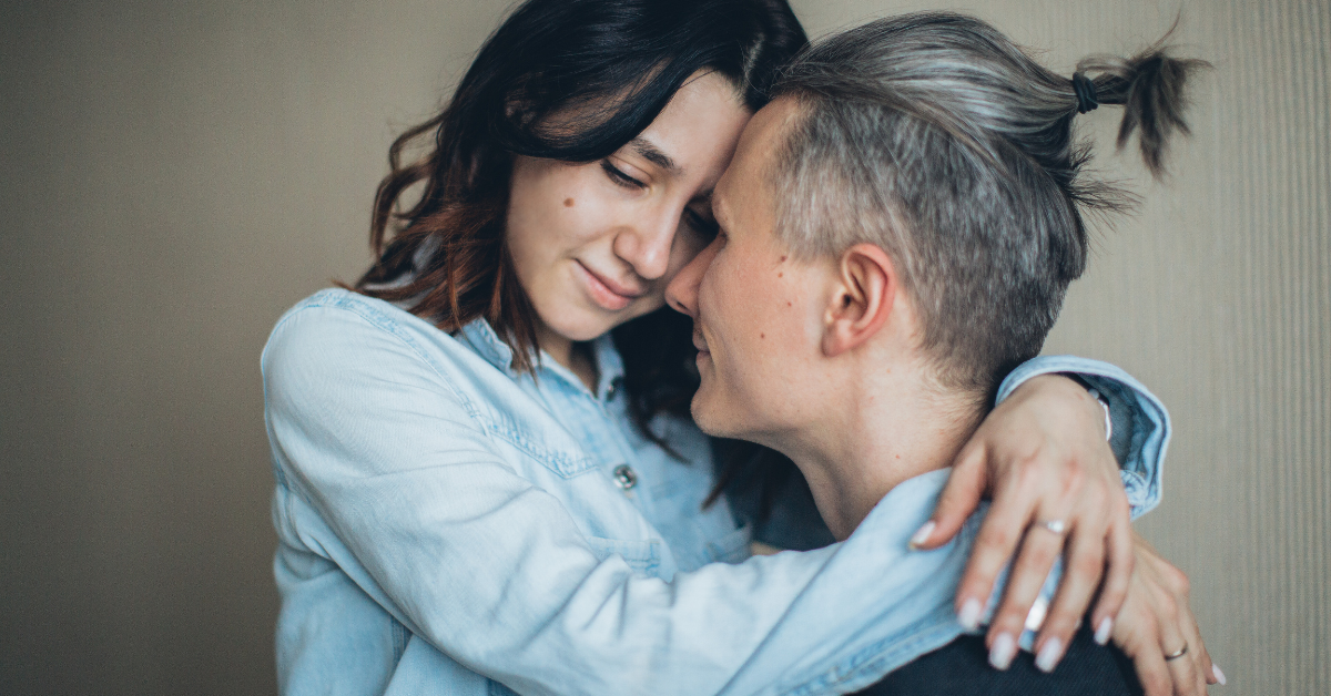woman wraps her arms around man's neck looking sad