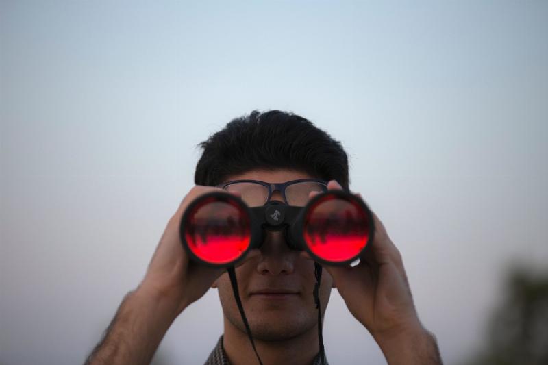 man holds up binoculars to his eyes