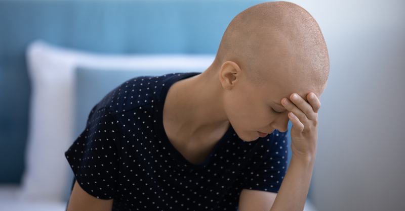 girl with shaved head sits looking sad