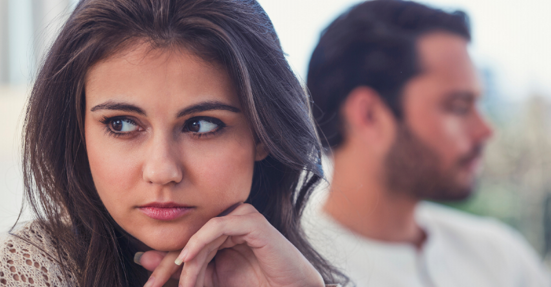 Upset woman looking off to the side with blurred man behind her
