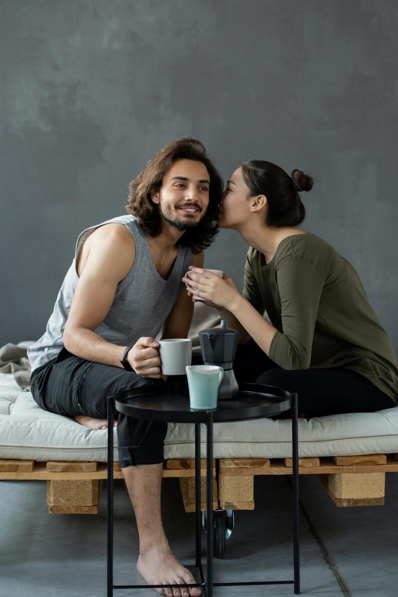 woman whispering into man's ear as they drink coffee