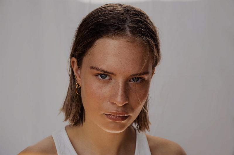 Portrait of a woman with freckles looking intently with a strand of hair falling over her eyes ad the rest tucked behind her ears