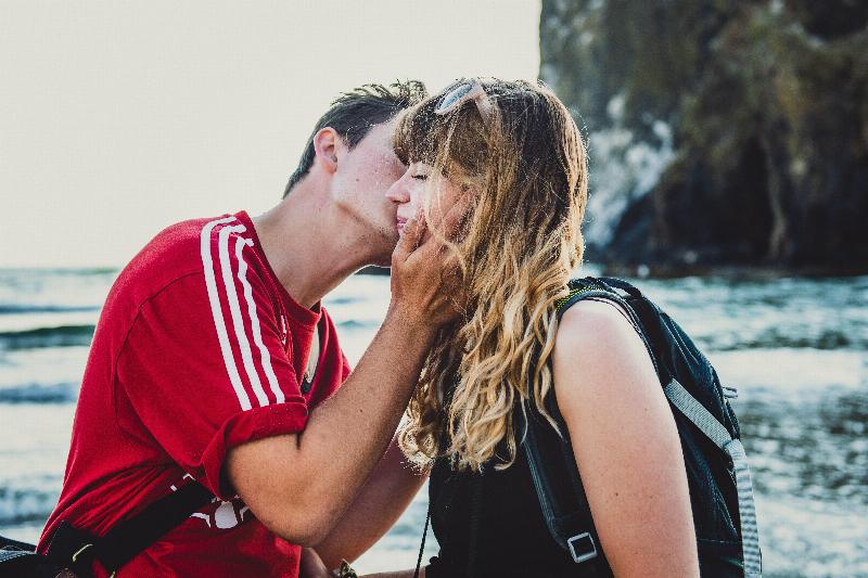 man grabs young woman's face to kiss her cheek by the water