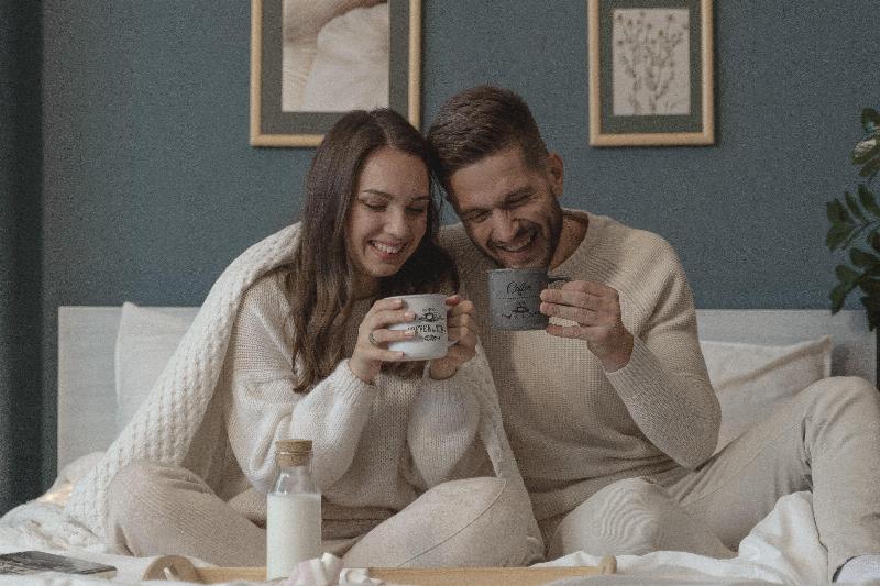 couple eating breakfast in bed and smiling wrapped in a blanket