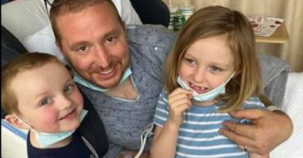 kyle holds his children for a picture in hospital bed