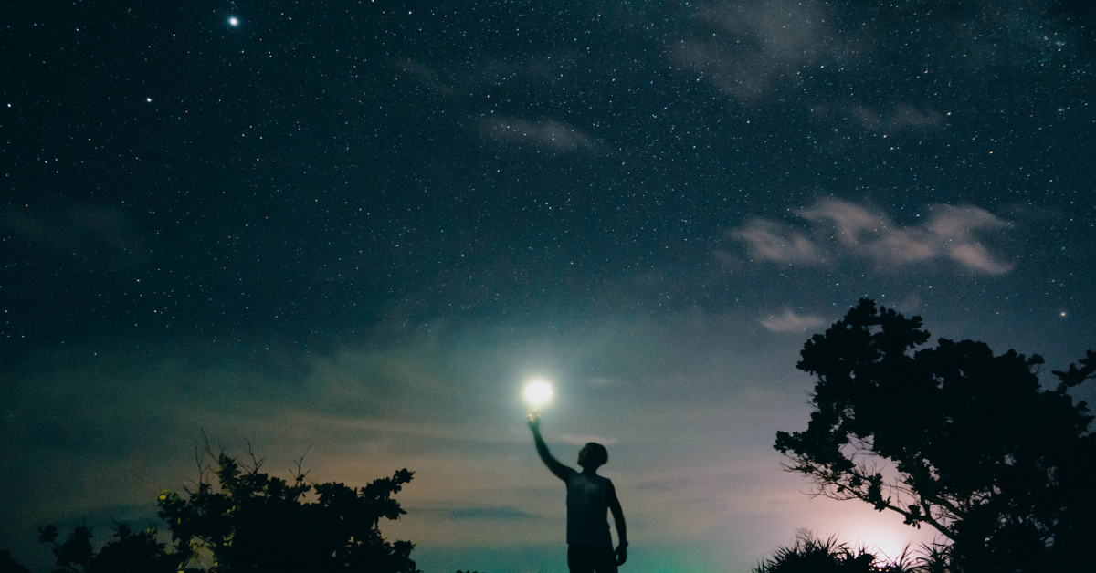 A person reaching for the bright moon in a star-filled sky. 