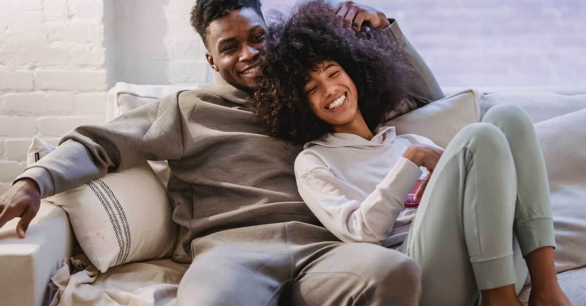 A man and woman smiling and cuddling on the couch.