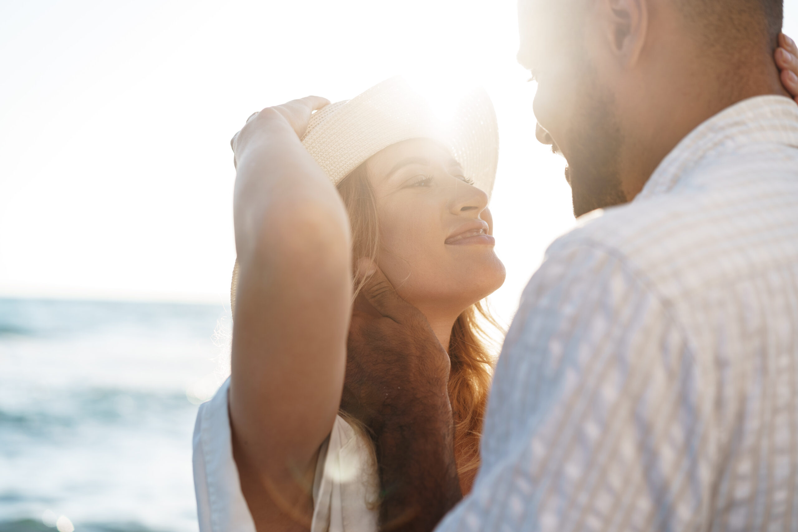 couple smiling at each other back lit by sun on beach 